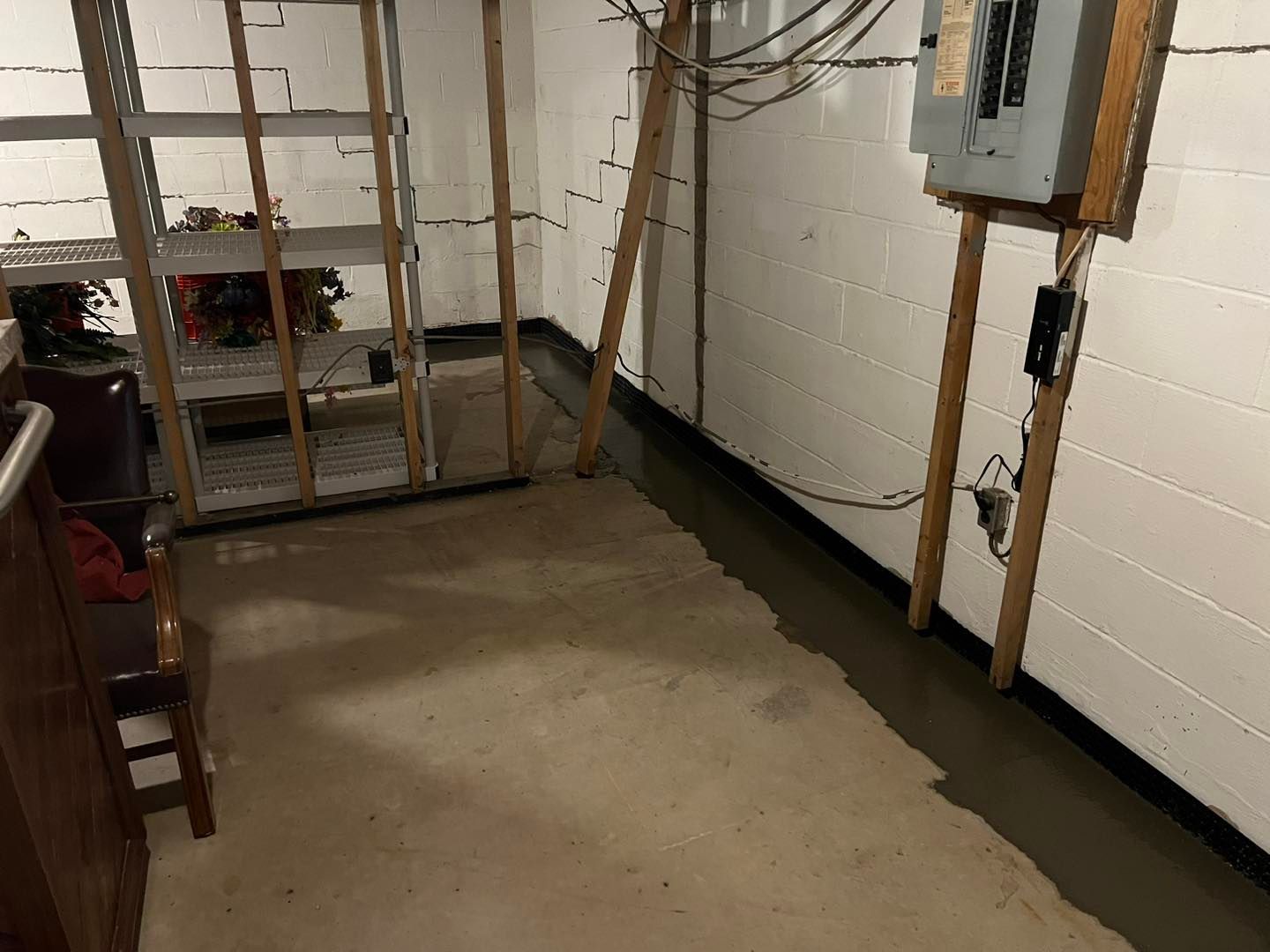 A basement with a ladder and a electrical box on the wall.