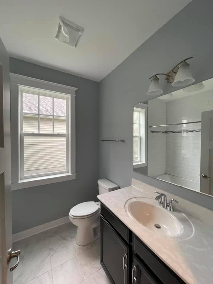 a bathroom with a toilet , sink , mirror and window .