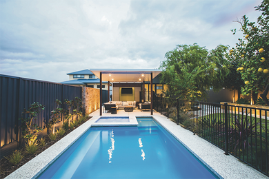 Long, rectangular pool with spa, surrounded by patio and fence, leading to a covered seating area.