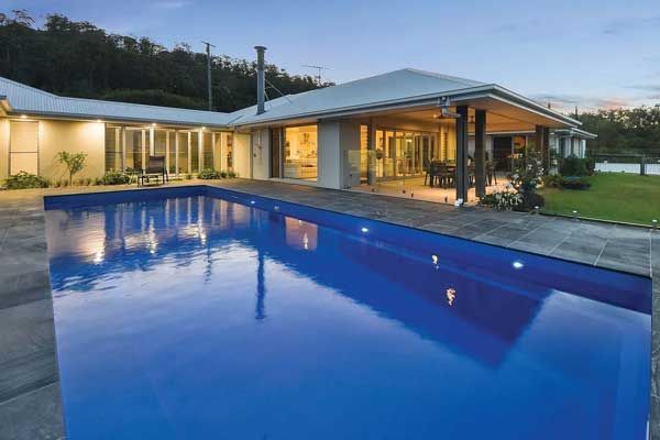 Luxurious house with a long blue pool in front. Evening setting, reflection of the house in the water.