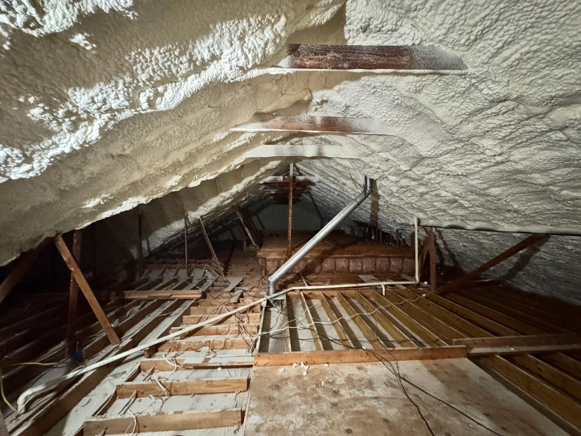 Interior of a damaged attic with exposed wooden rafters and collapsed insulation.