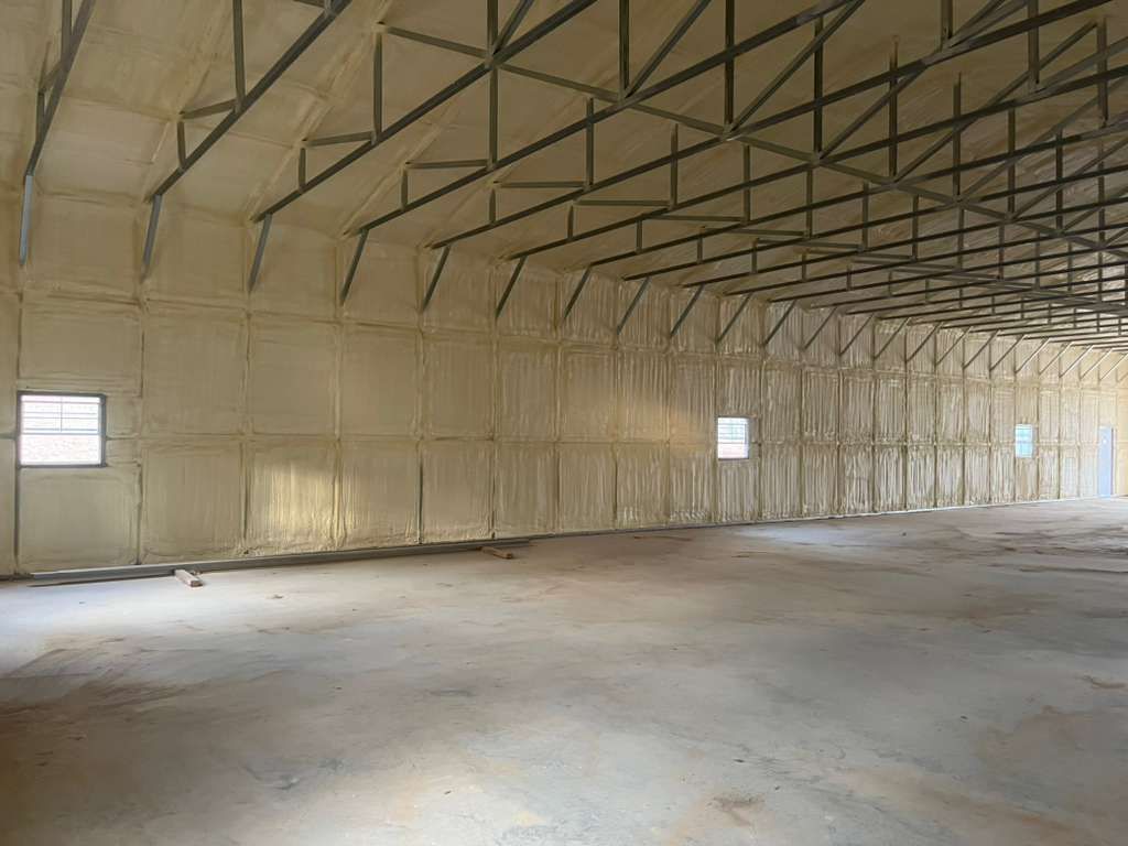 Empty warehouse interior with metal trusses, white insulated walls, and small windows.