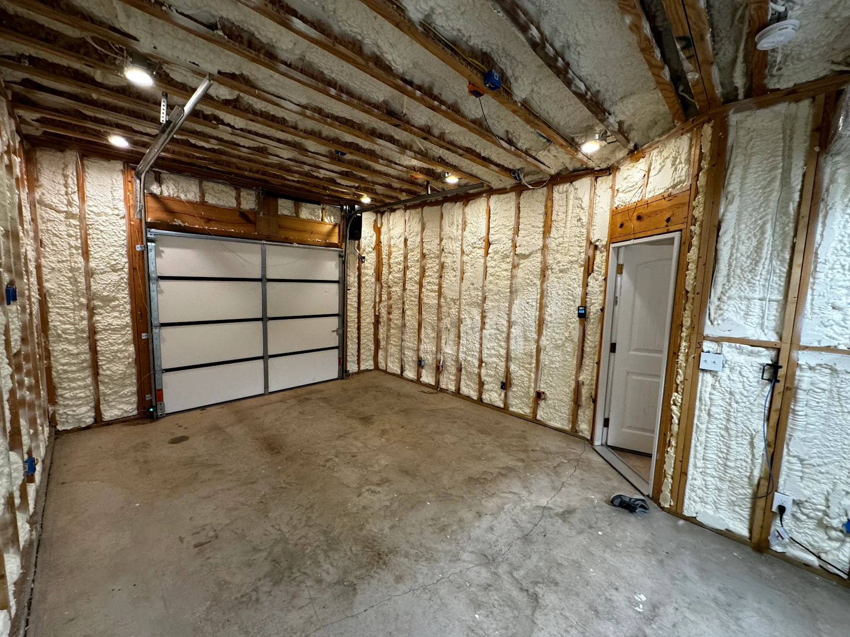 Empty unfinished garage interior with exposed insulation, concrete floor, and a white garage door.