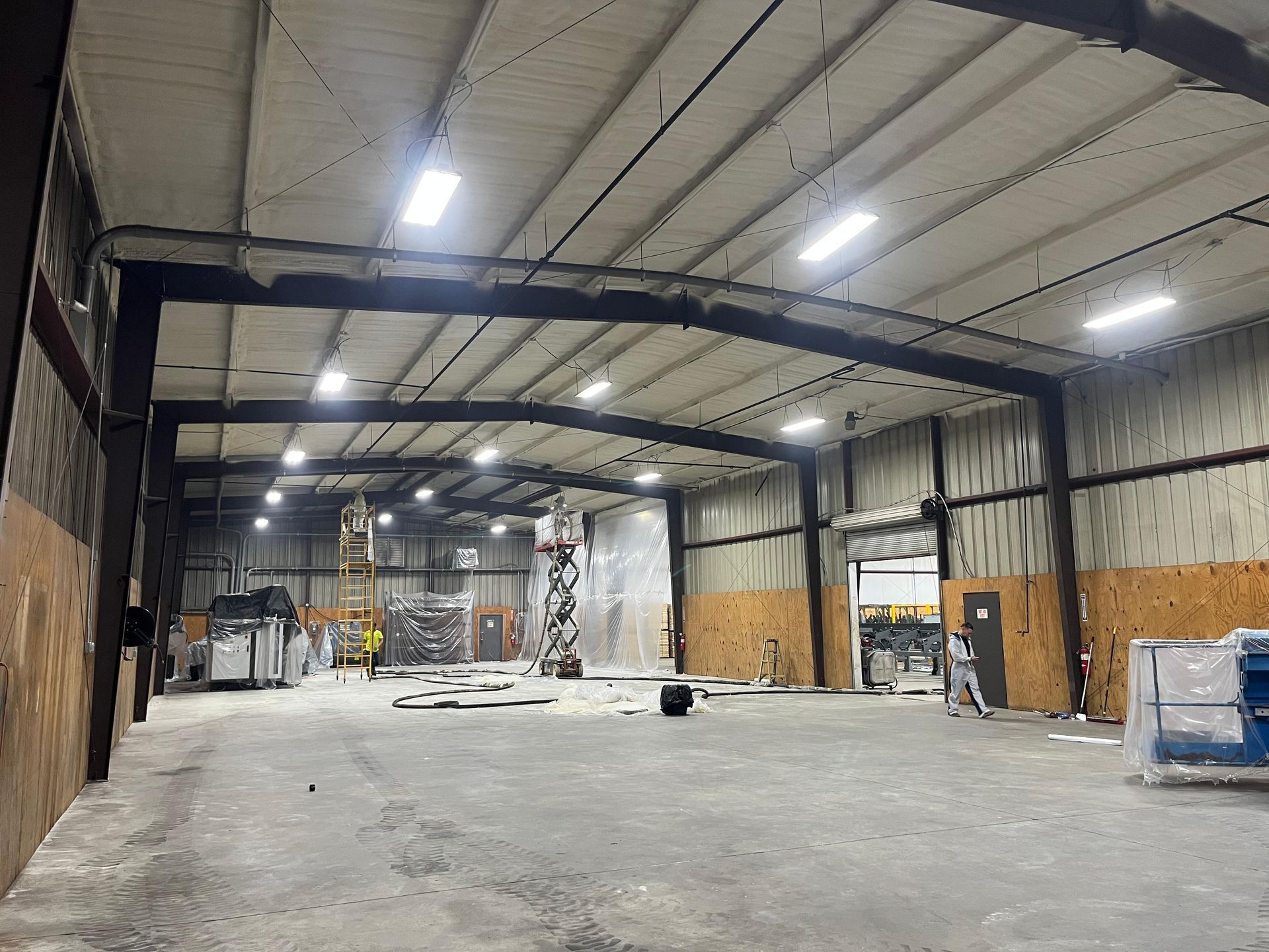 Empty warehouse interior with high ceiling, concrete floor, and scattered construction materials