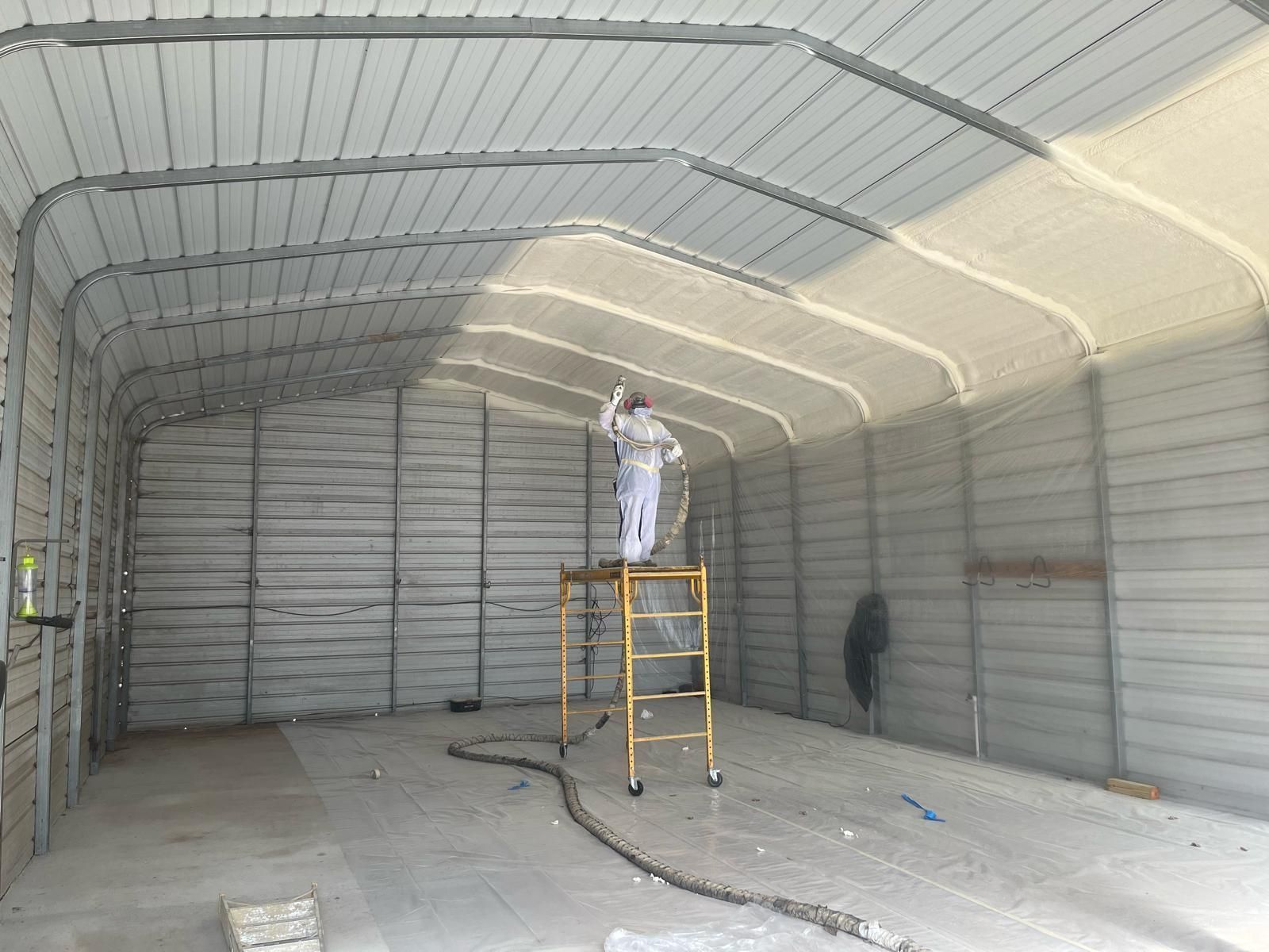 Person on a yellow ladder painting the ceiling of a large empty metal garage.