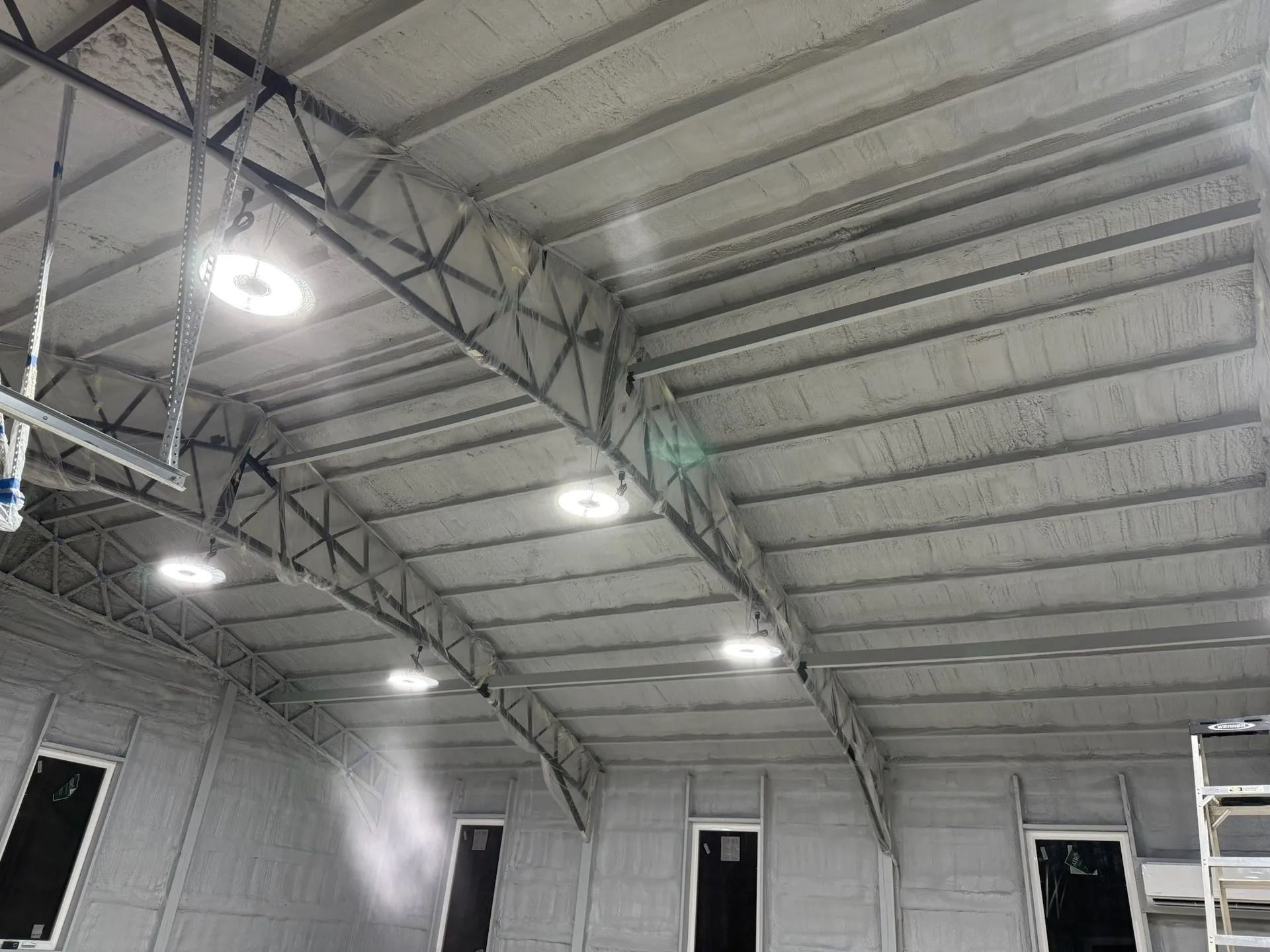 Interior of a large white metal warehouse ceiling with hanging lights and beams