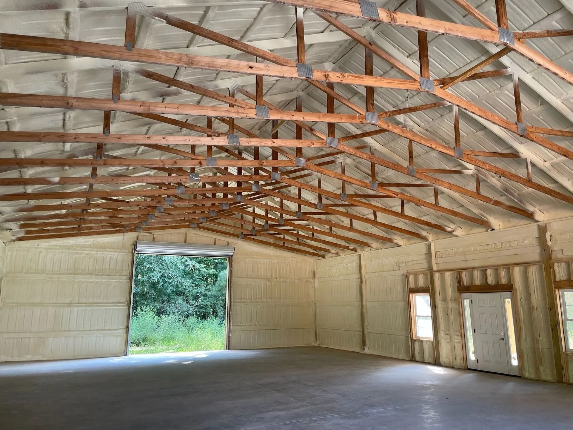 Empty metal barn interior with exposed roof trusses and an open doorway to greenery