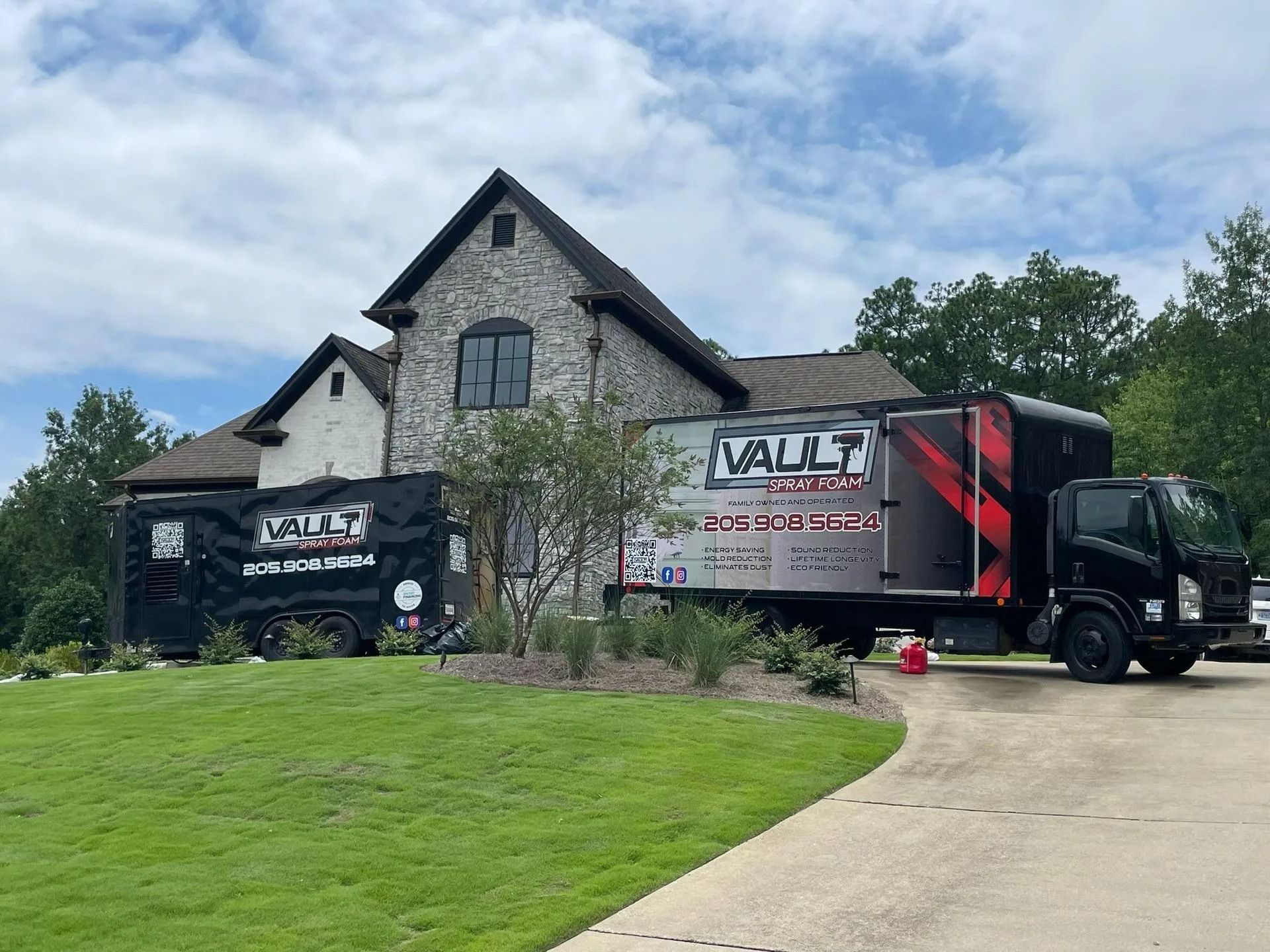 Delivery truck parked beside stone house on a driveway, with green lawn and cloudy sky.