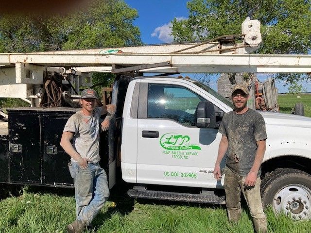 Two workers standing beside a white utility truck with an extended boom in a grassy outdoor area.
