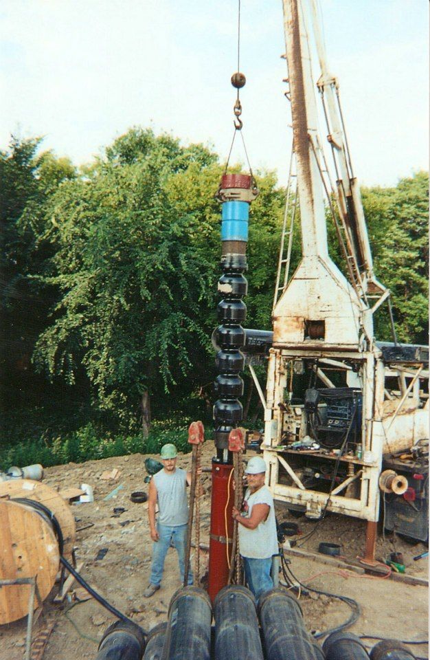 A man is standing next to a crane that is lifting a large pipe