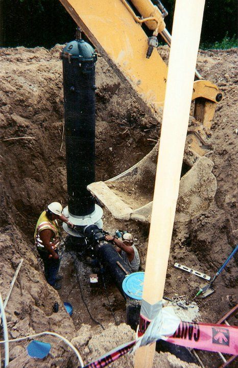 Construction workers are working in the dirt near a yellow excavator