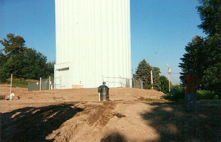 A man is standing in the dirt in front of a large white building