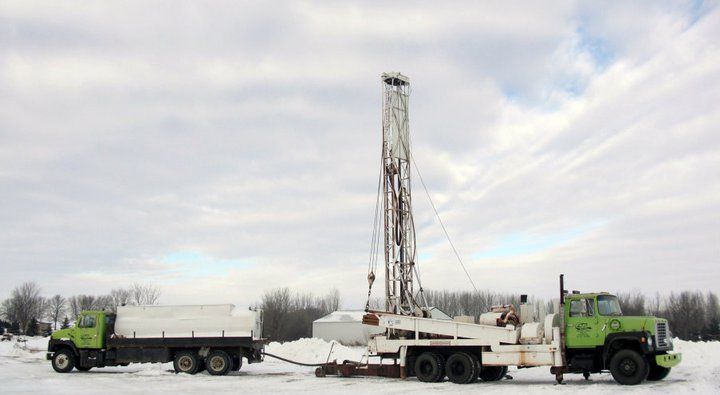 A green and white truck with a drilling rig attached to it