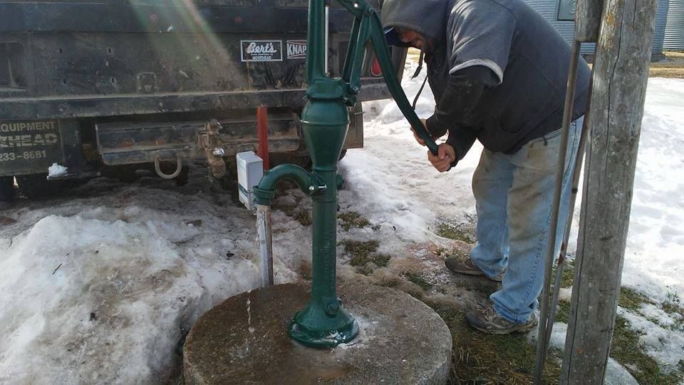 A man is pumping water from a well in the snow.