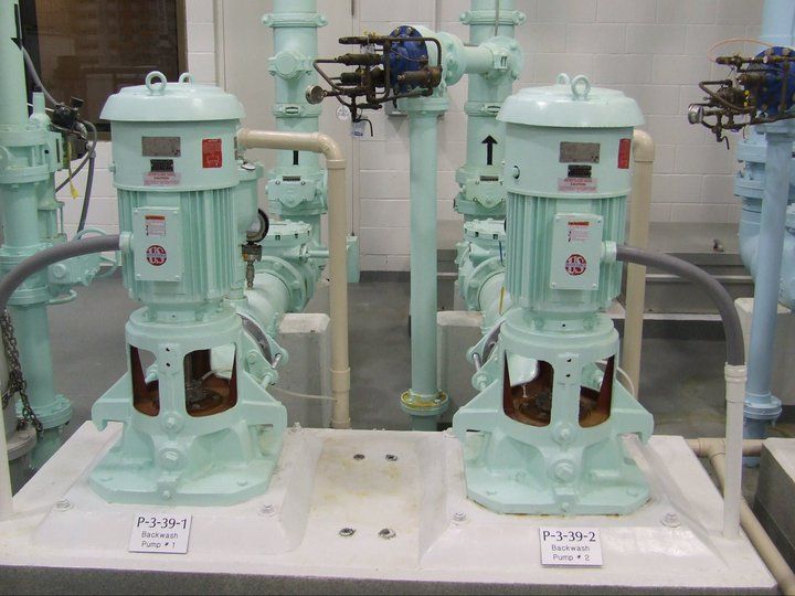 Two green pumps are sitting next to each other in a room with pipes.