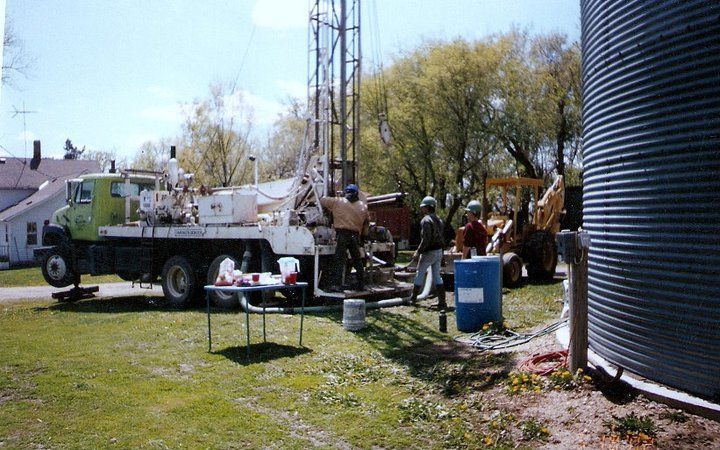 A truck is parked in a grassy field next to a water tank.