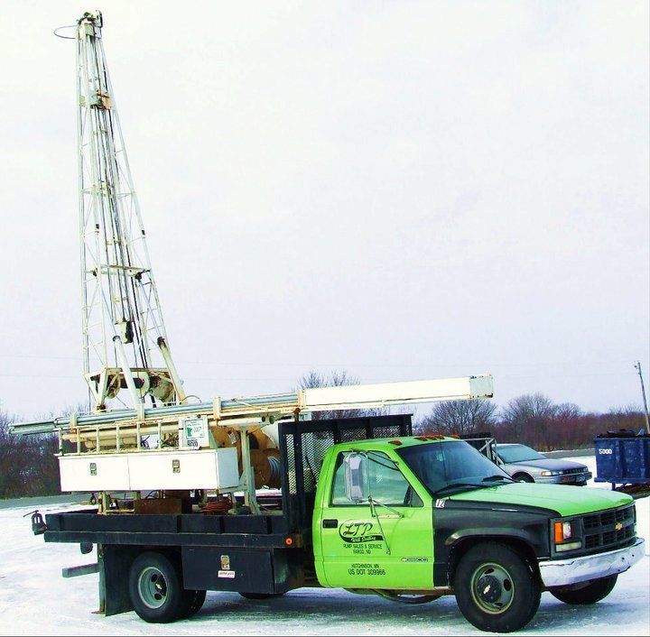 A green truck with a crane on the back is parked in the snow