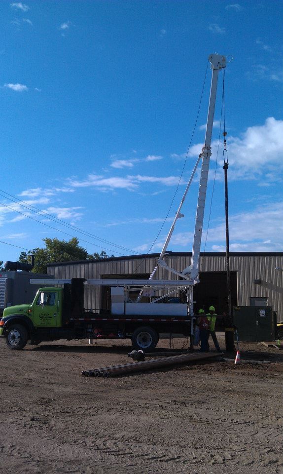 A green truck is parked in a dirt lot next to a crane.
