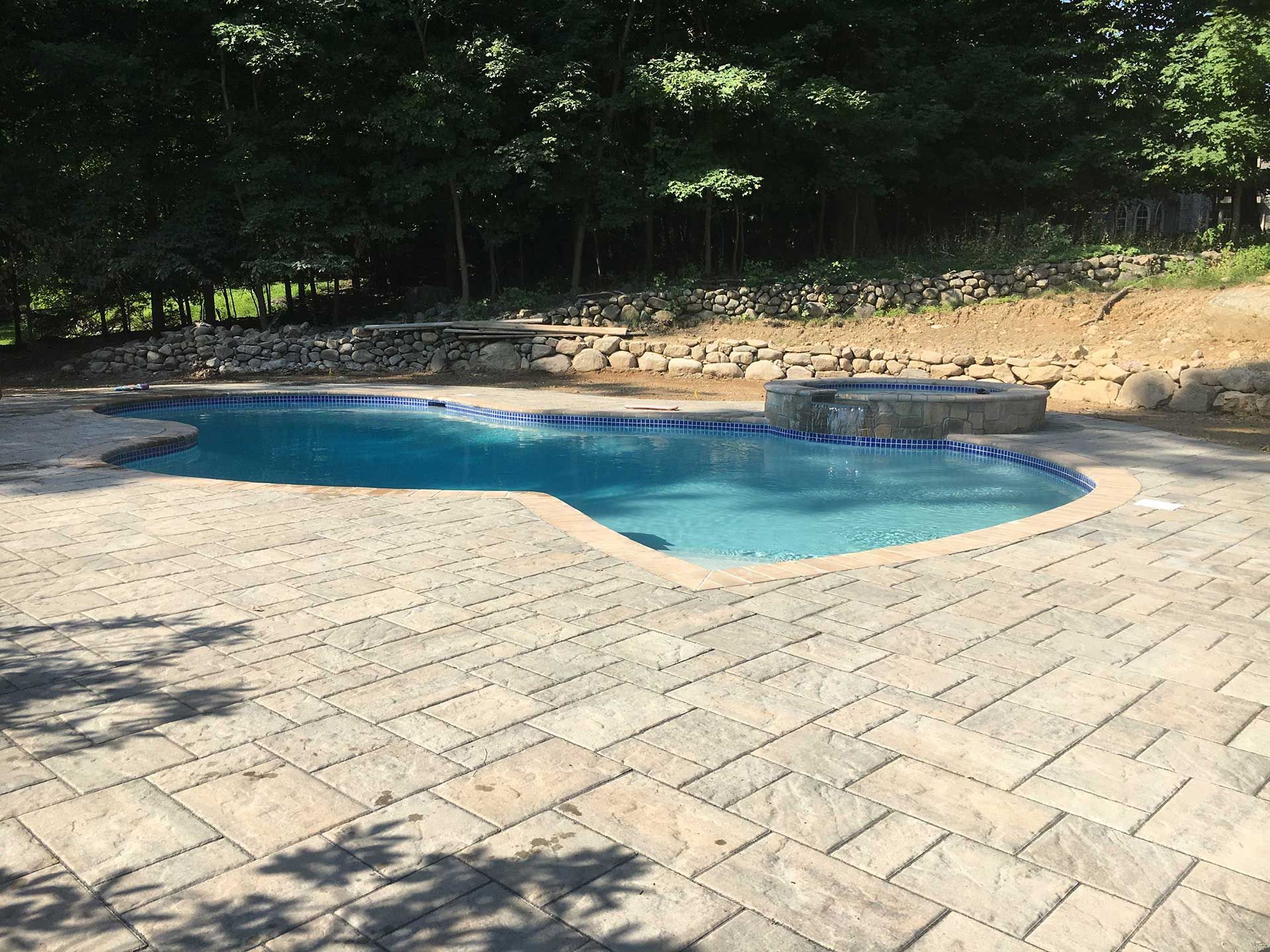 A large swimming pool is surrounded by a brick patio
