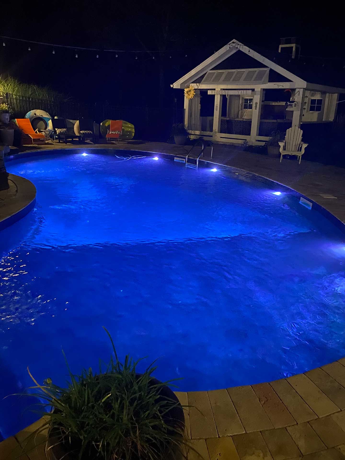 A large swimming pool is lit up at night with blue lights