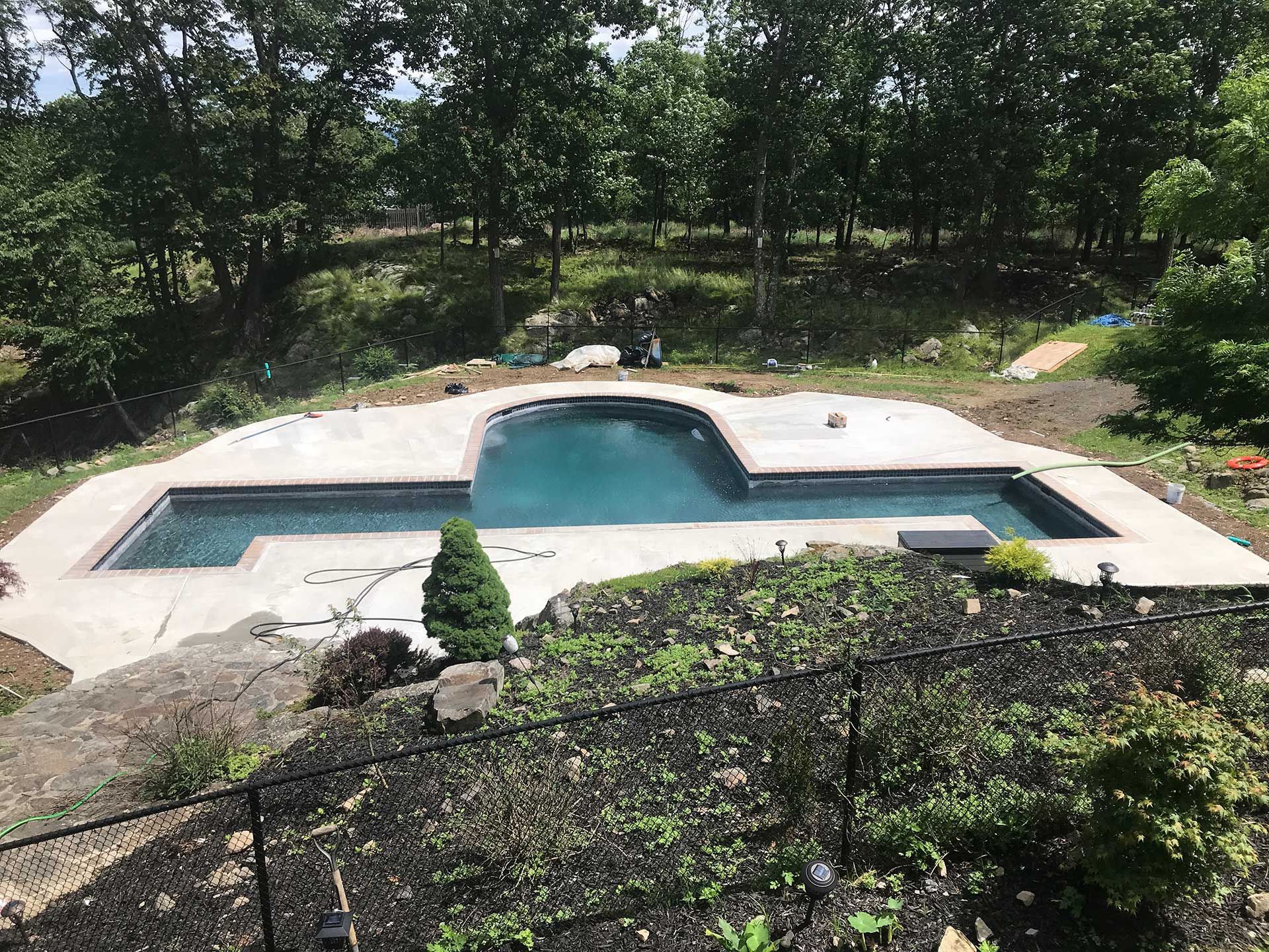 A large swimming pool is surrounded by trees and a fence