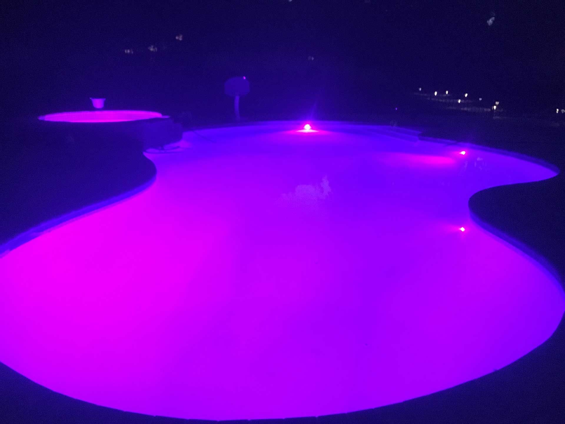 A swimming pool is lit up with purple lights 