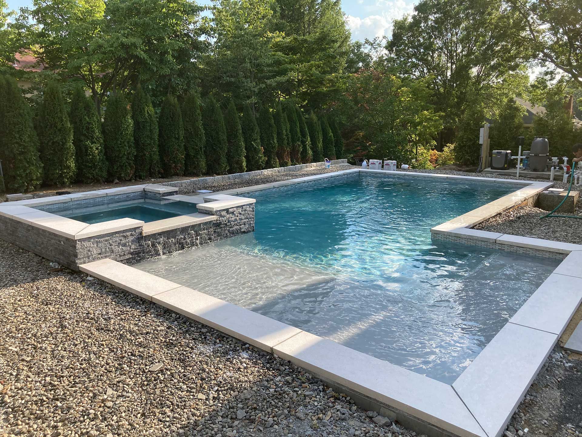 A large swimming pool with a hot tub in the backyard surrounded by trees