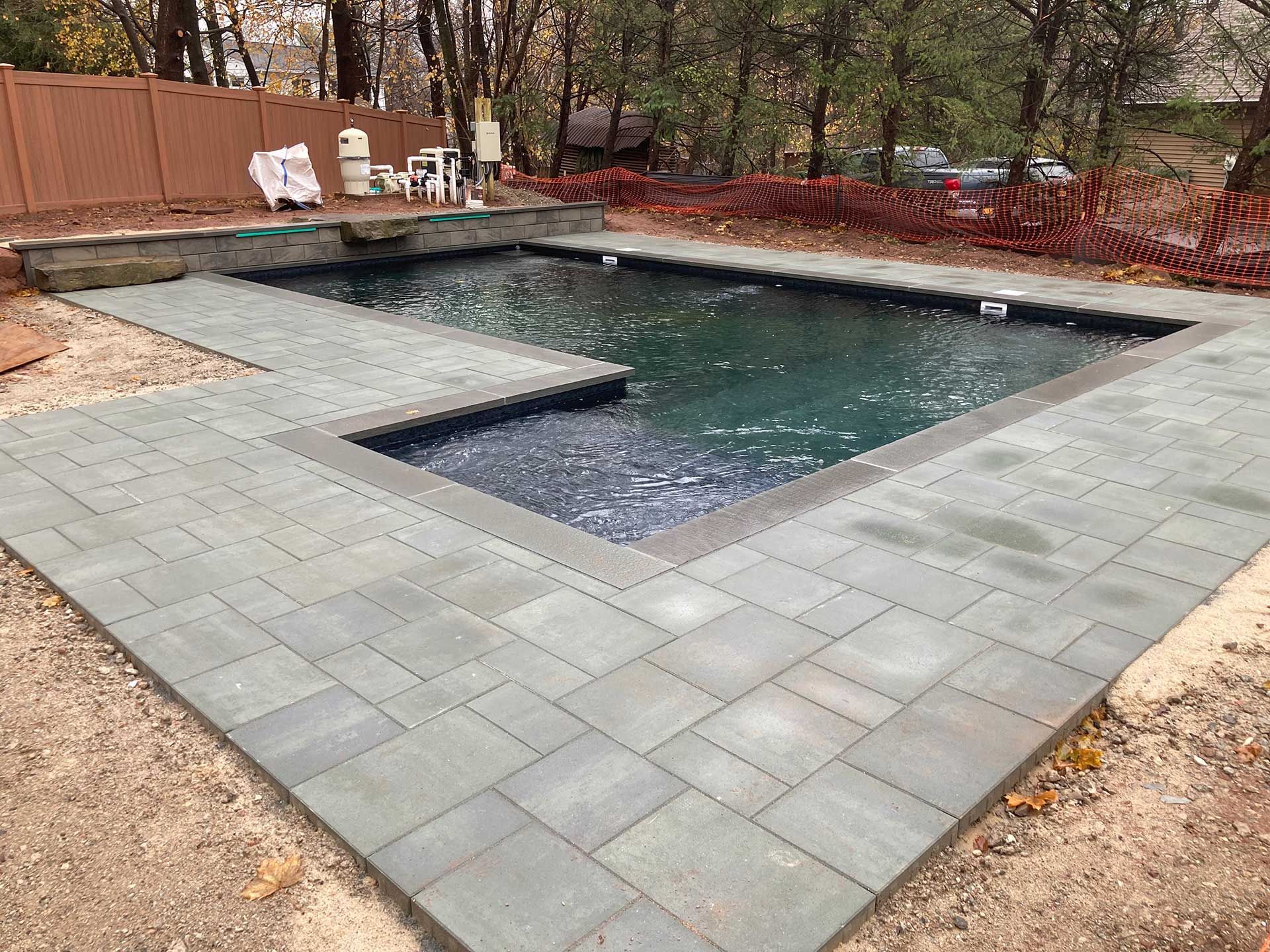 A large swimming pool is surrounded by a patio and a fence