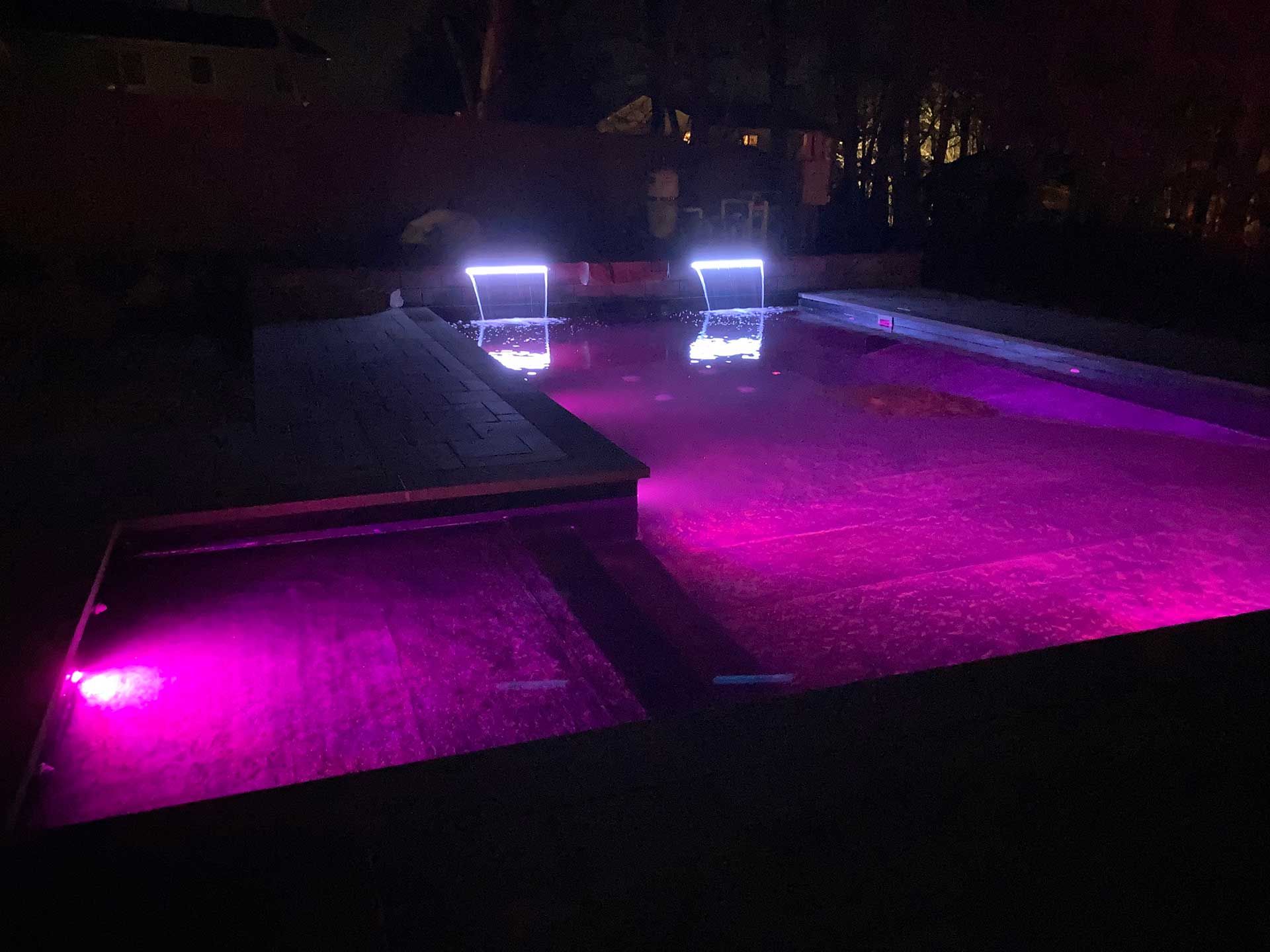 A swimming pool is lit up with purple lights at night
