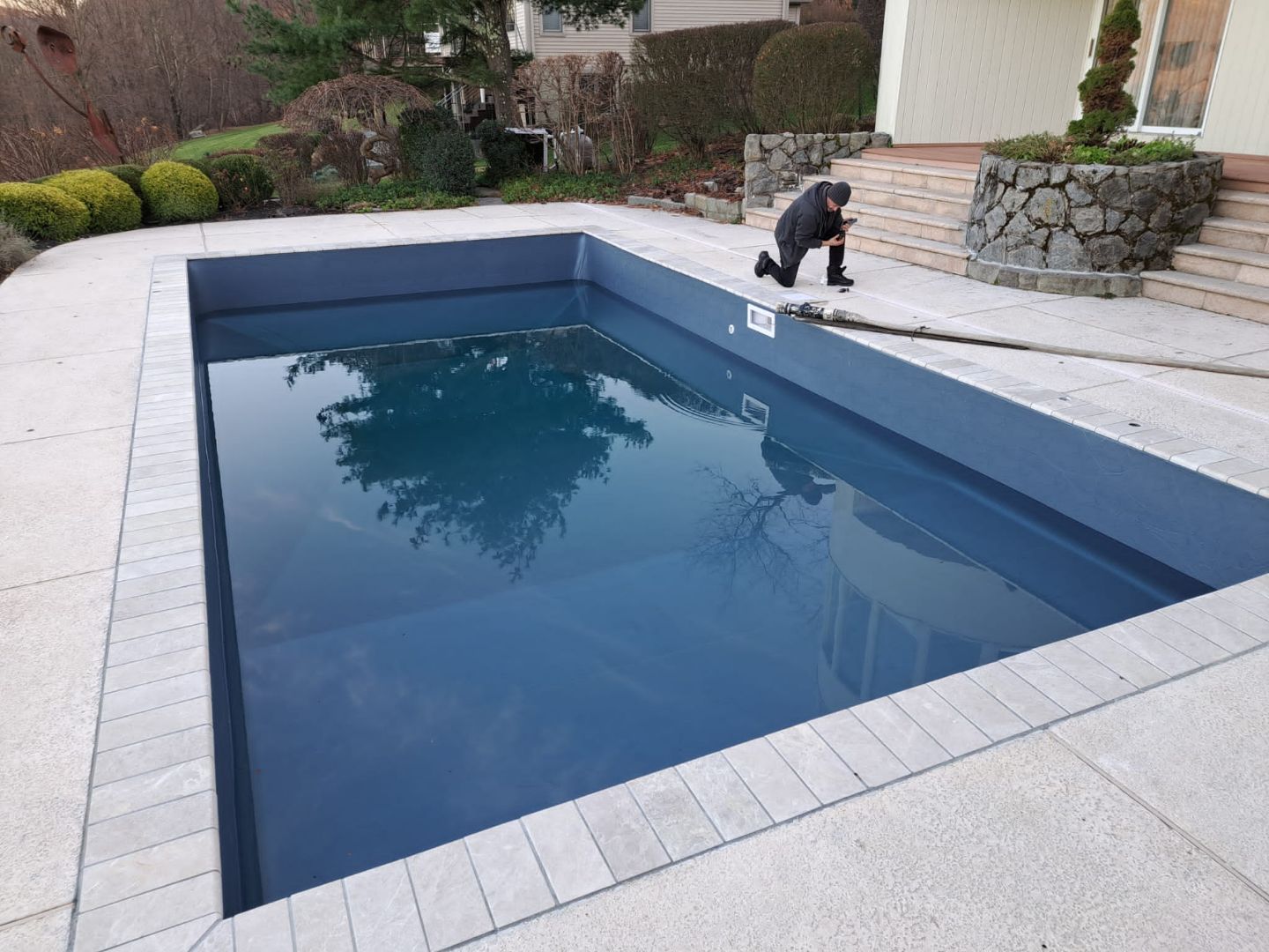 A man is kneeling in front of a large swimming pool