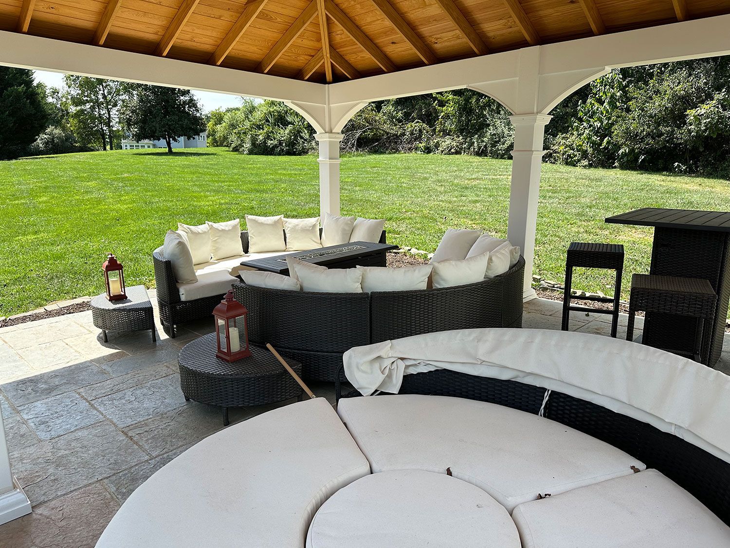 Gazebo with outdoor seating on a stone patio overlooking a green lawn.