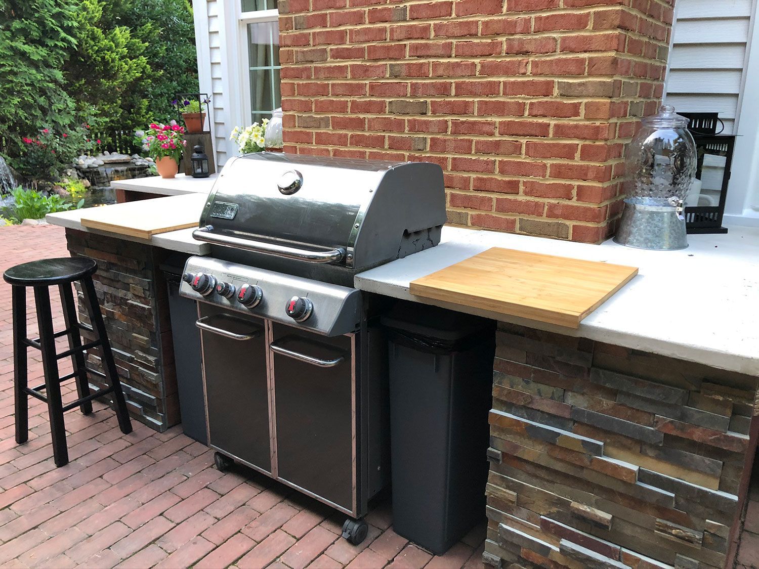 Outdoor kitchen with a stainless steel grill, brick backdrop, and stone facade.