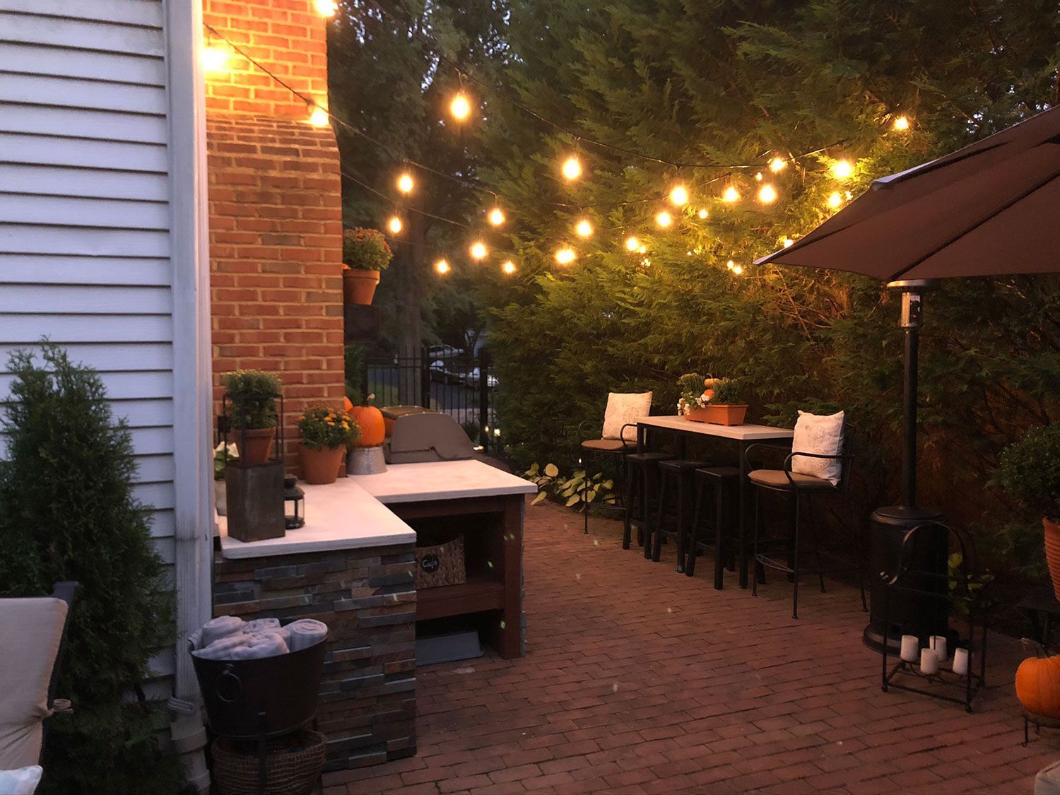 Outdoor patio with string lights, brick patio, bar seating, and pumpkins.