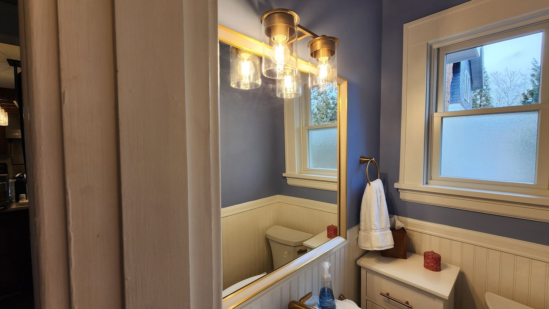 A bathroom with a toilet , sink , mirror and window.
