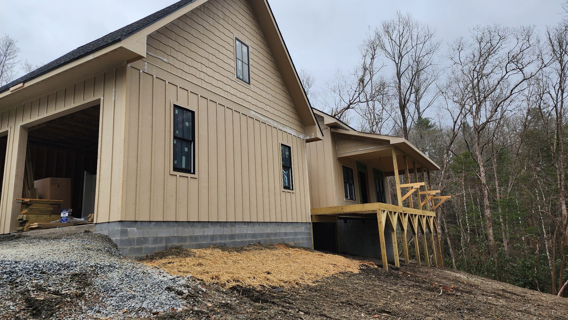 A house is being built in the woods with a garage and a porch.