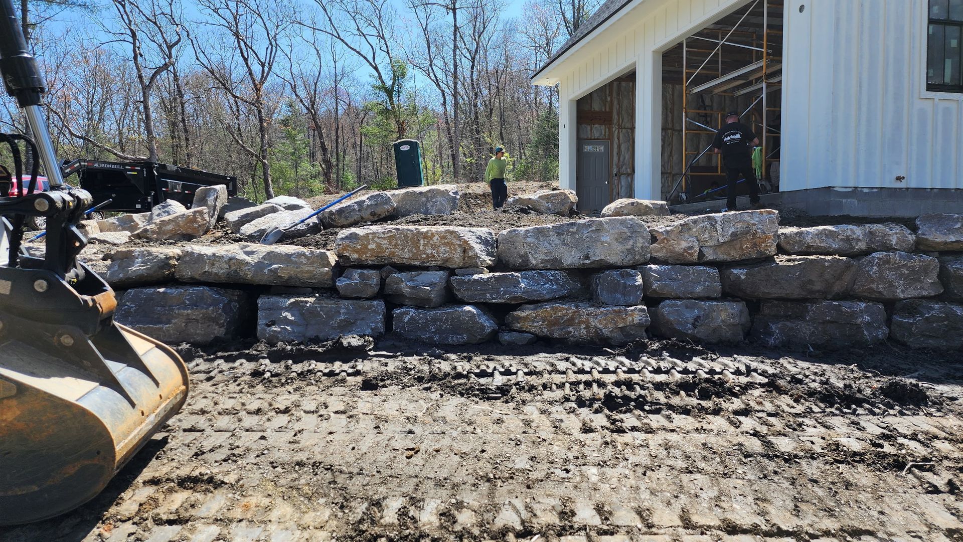 A bulldozer is working on a stone wall in front of a house.