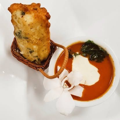 Fried pastry in a basket beside a white bowl of red sauce with cream and greens