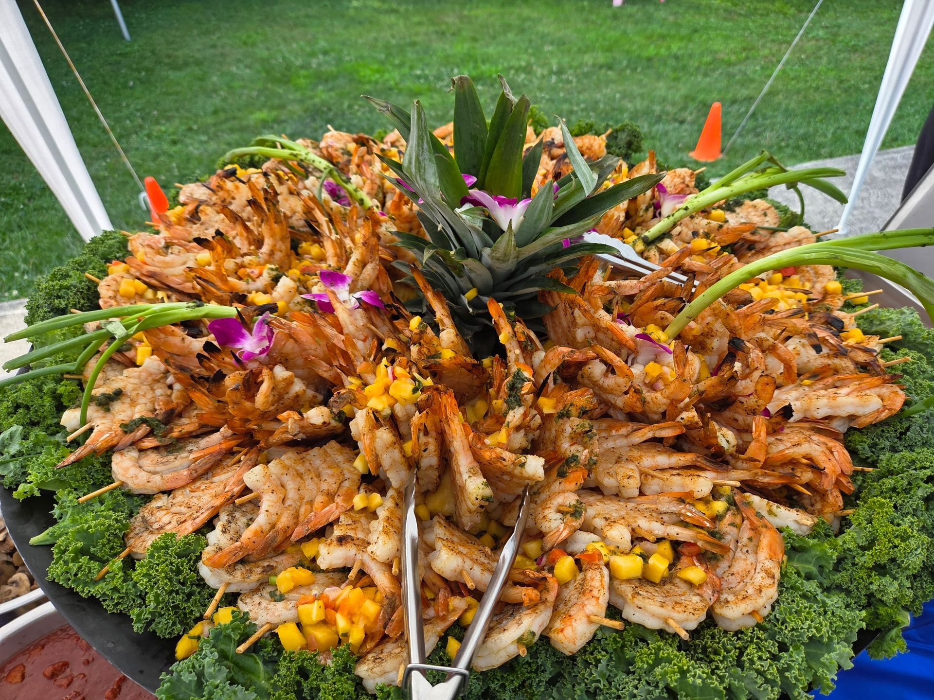 Large seafood platter with shrimp, mussels, fruit garnish, and pineapple centerpiece on a green lawn