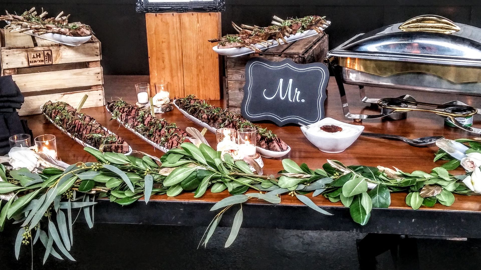 Buffet table with carved meats, leafy greens, and serving trays under a chalkboard sign