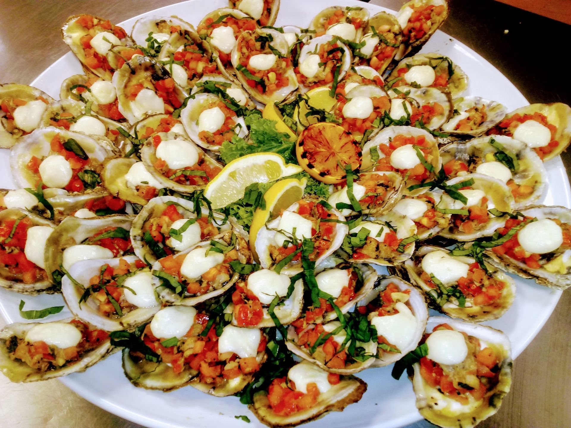 Plate of bite-sized appetizers topped with herbs, tomatoes, and mozzarella, arranged in a floral pattern with lemon wedges