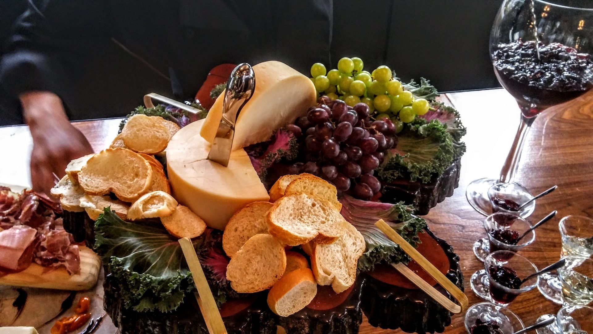 Wine and fruit cheese platter with crackers on a table, featuring grapes, pears, and sliced bread