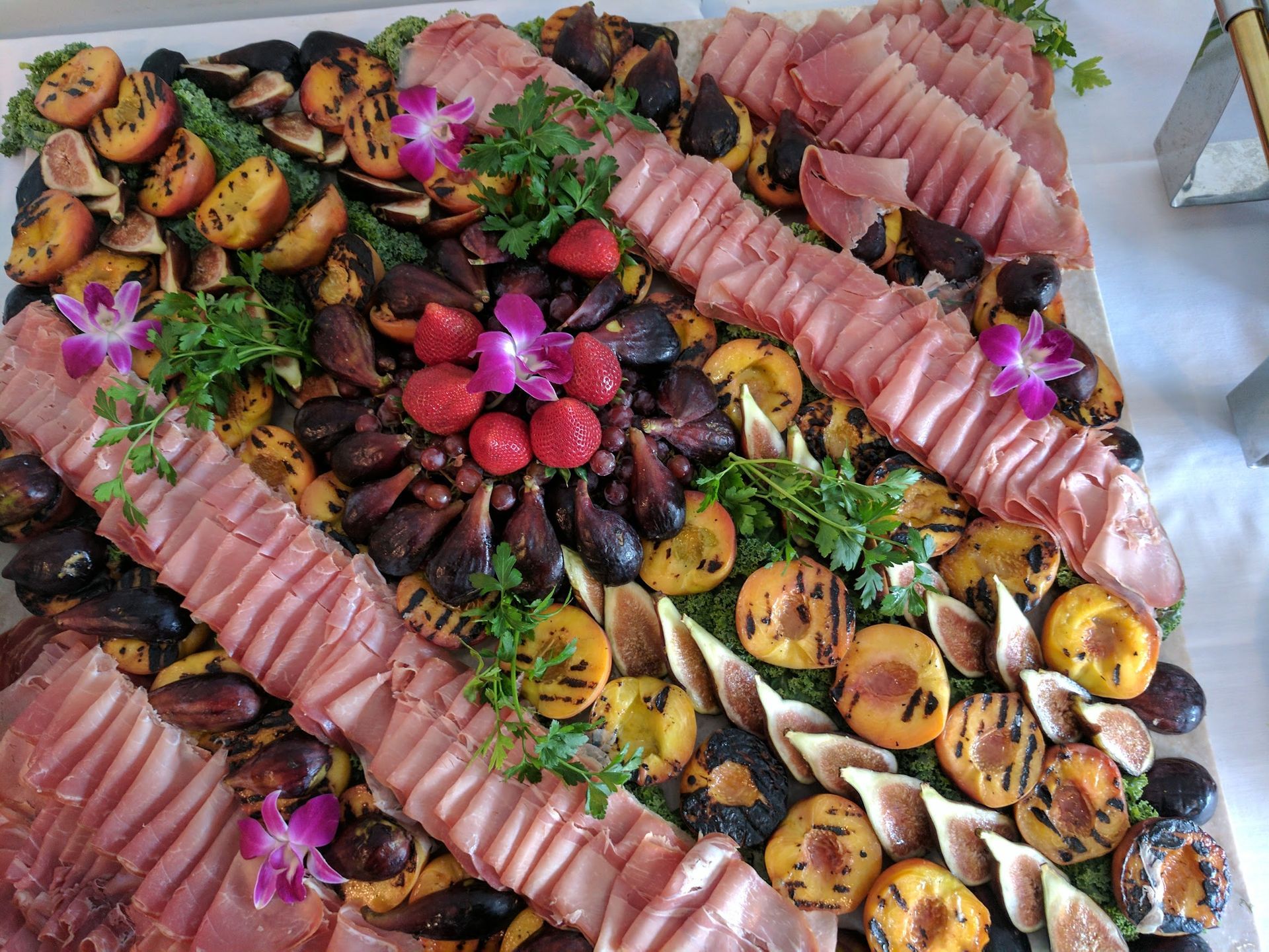 Platter of sliced cured meat, charcuterie, and flowers arranged on a table