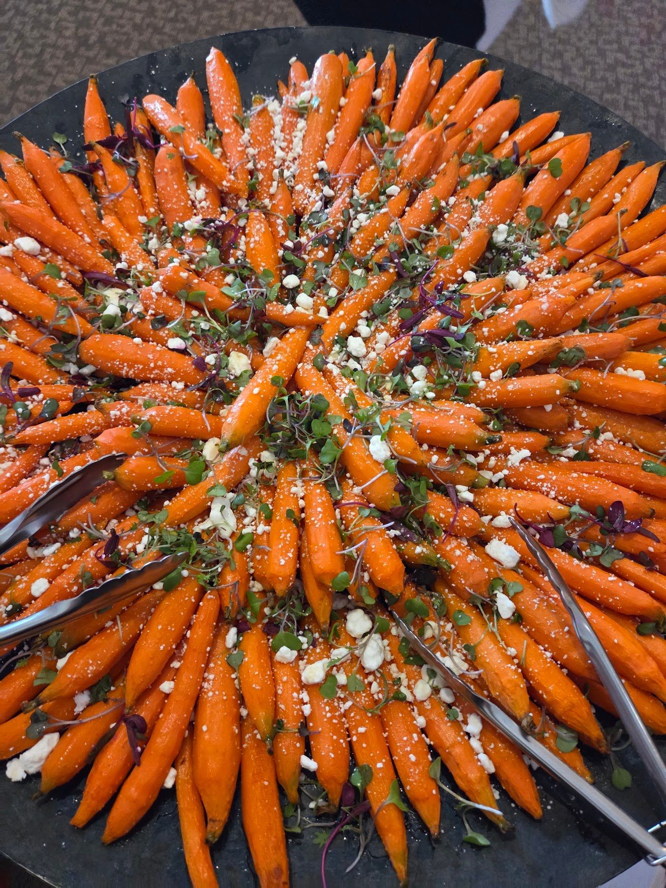 Tray of orange carrots arranged in a circular pattern with chopped herbs and seasoning on top