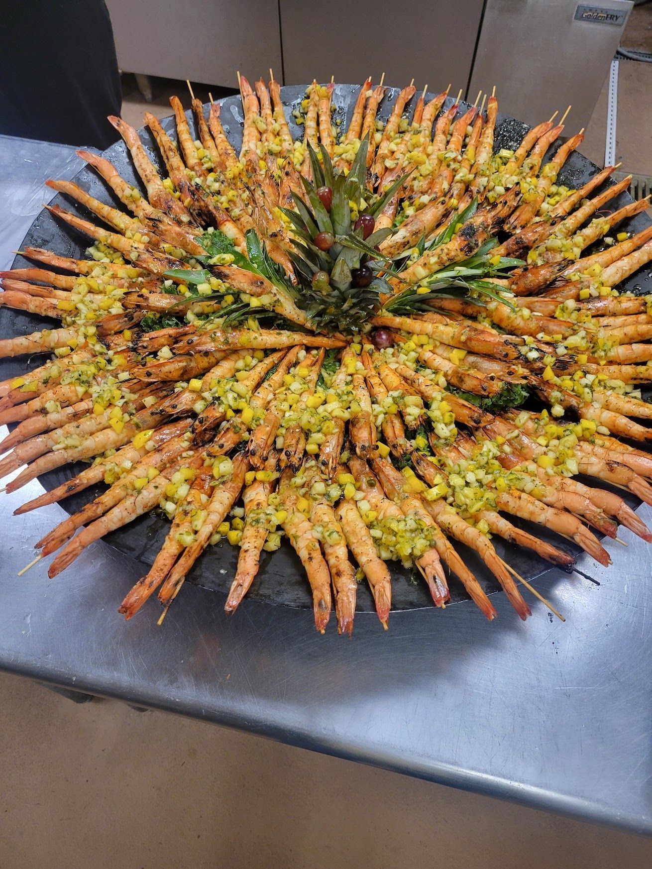 Circular platter of grilled shrimp arranged in a sunburst pattern on a dark table