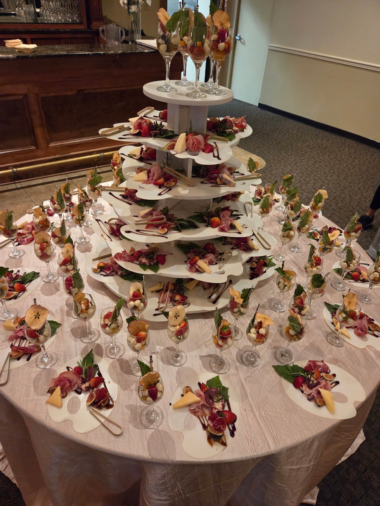 Round dessert table display with tiered plates of decorated pastries and small flower arrangements on white tablecloth