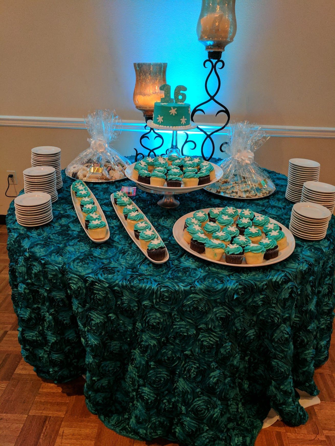 Teal-themed dessert table with cupcakes, cake pops, and candles on decorative stands