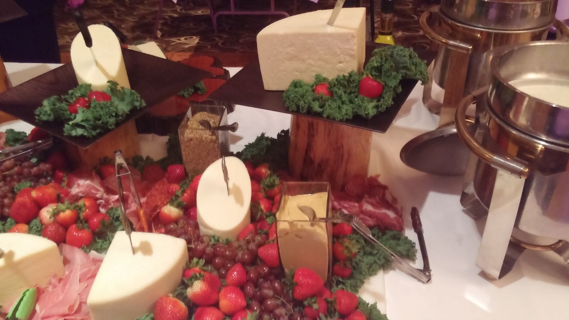 Buffet table with strawberries, cheese wedges, greenery, and silver serving trays