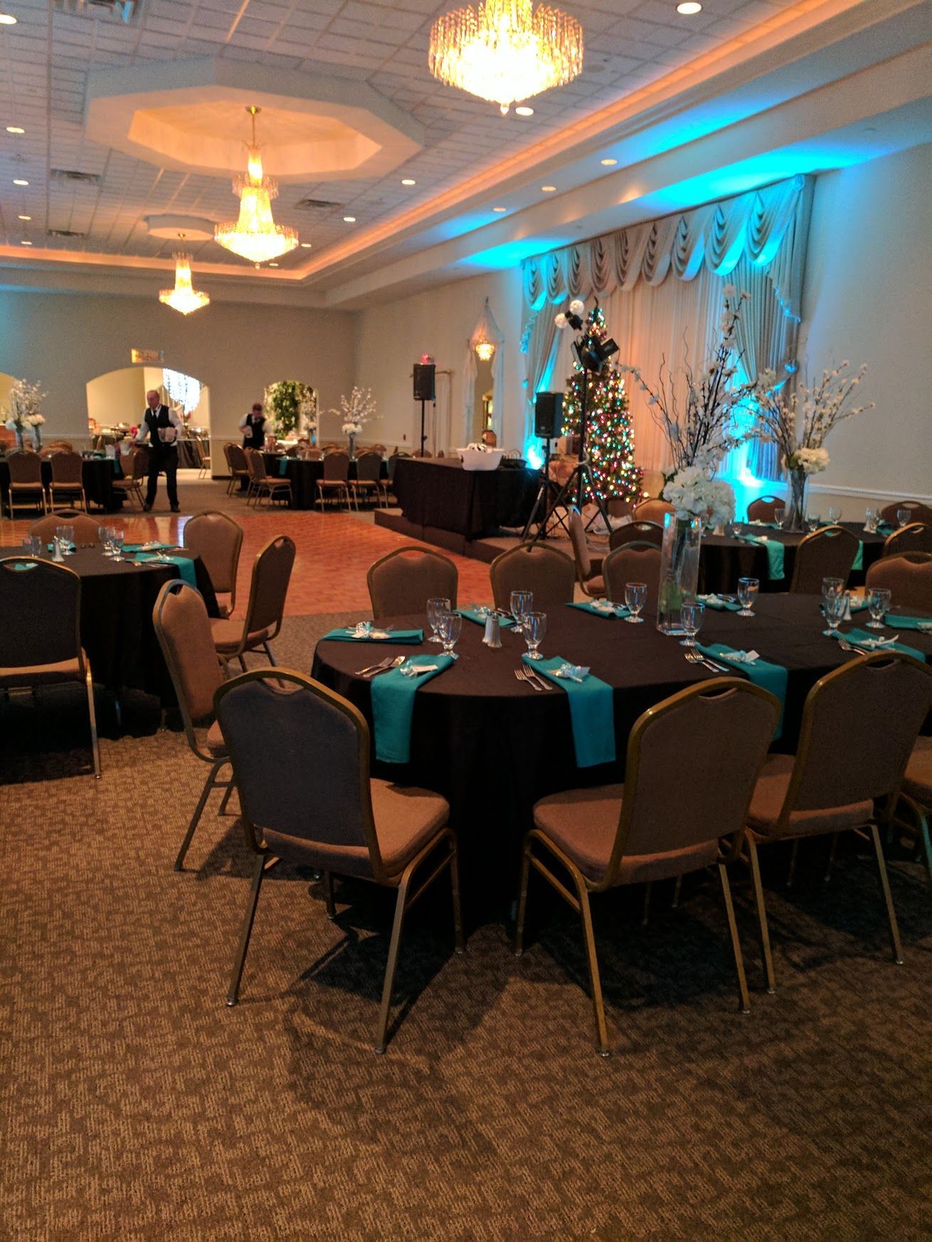 Banquet hall with round tables, teal chairs, chandeliers, and blue uplighting along the walls.