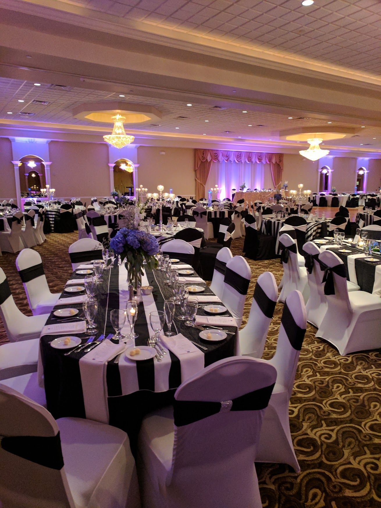 Elegant banquet hall with round tables dressed in black-and-white linens and purple uplighting