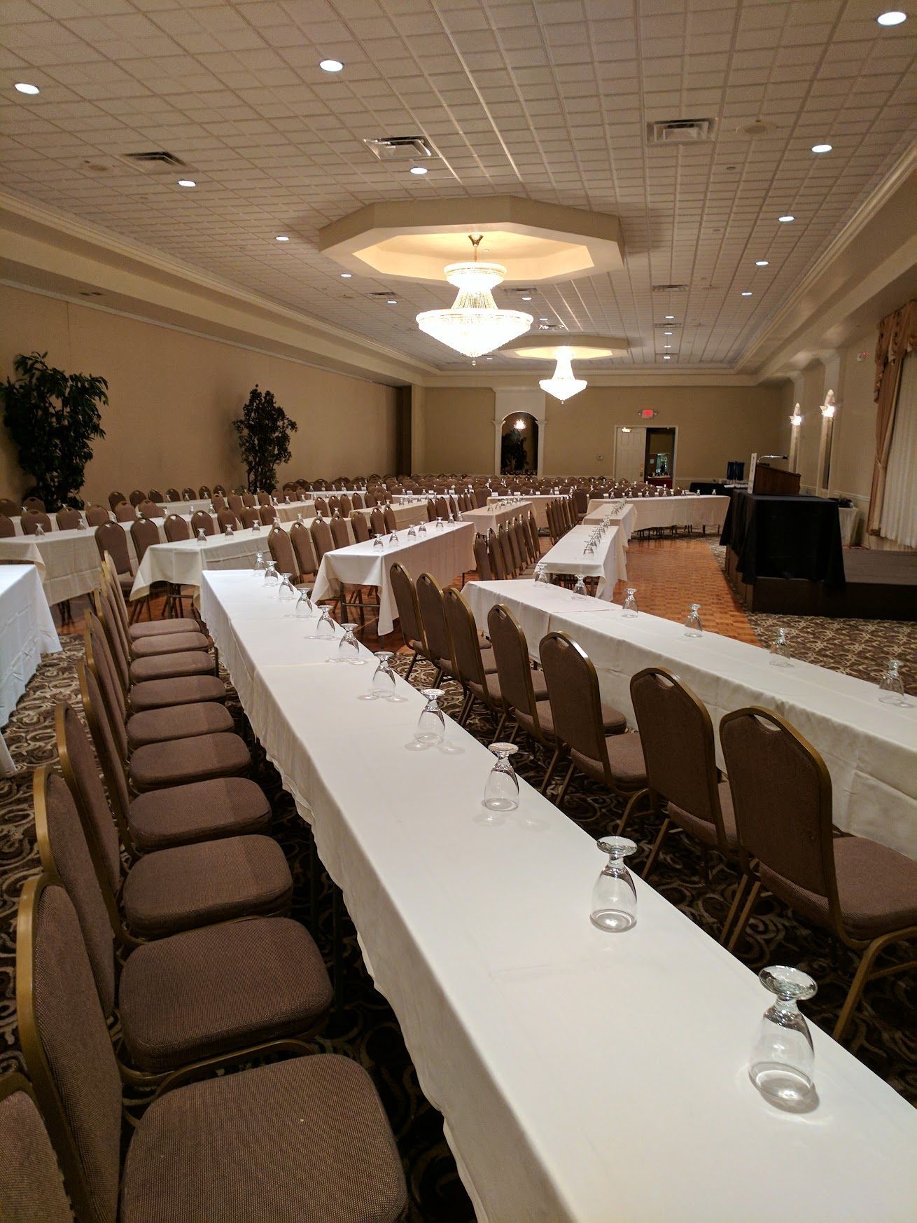 Empty banquet hall with U-shaped tables, brown chairs, and chandeliers under a patterned ceiling
